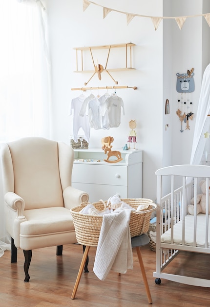 Scandinavian style white interior  bedroom, nursery. Baby cot with âcanopy. Wooden shelves and toys. Armchair in children's room