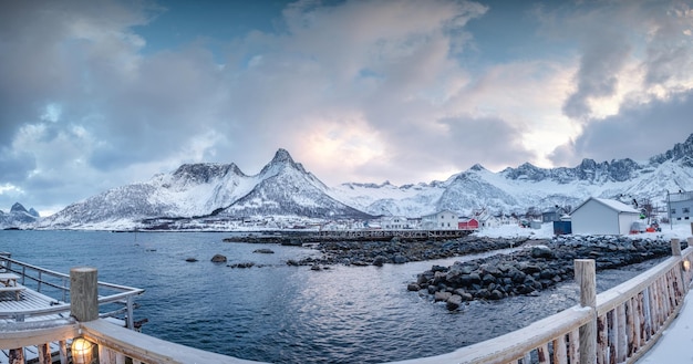 Scandinavian village with snow covered mountain range on coastline in winter at Mefjord Brygge Senja Island