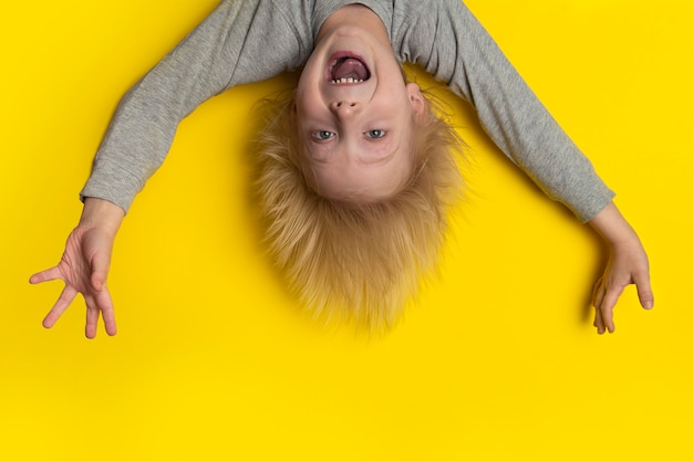 Photo scared boy with blond long hair hangs upside down and shouts.