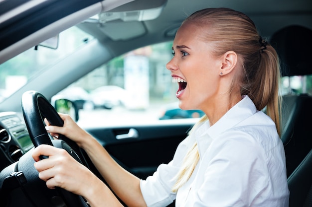 Scared business woman driving her car and shouting