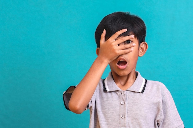 Scared frightened Asian boy looking at camera through fingers, closing eyes in shock