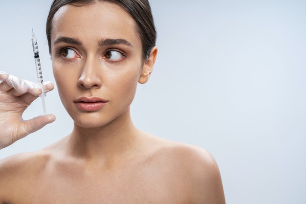 Scared girl is ready for beauty procedures against light background