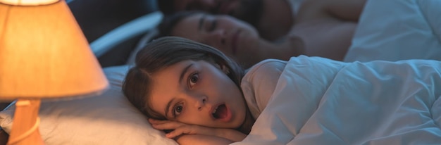 The scared girl lay near the sleeping parents in the bed night time