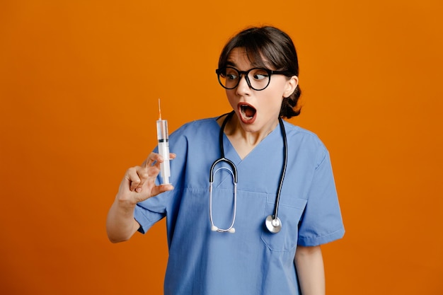 scared holding syringe young female doctor wearing uniform fith stethoscope isolated on orange background