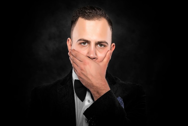 Scared man in suit hand covering mouth over dark background.