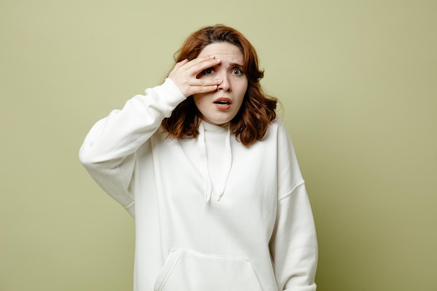 Scared putting hand on head young female wearing white sweater isolated on green background