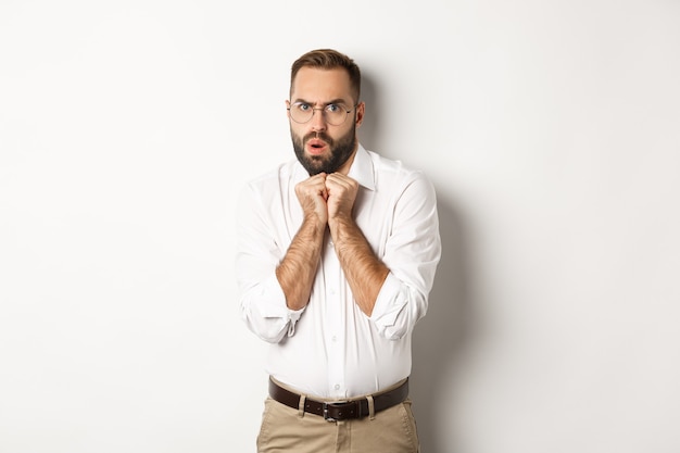 Scared and timid businessman looking anxious, trembling from fear, standing over white background.