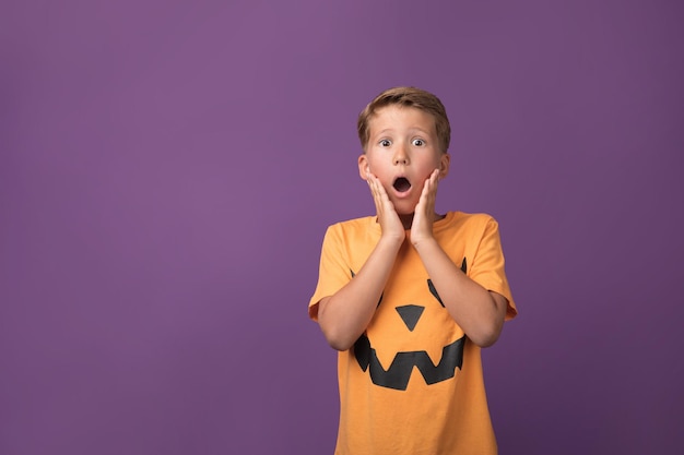 Scared young boy in Halloween outfit posing on purple background Studio shot