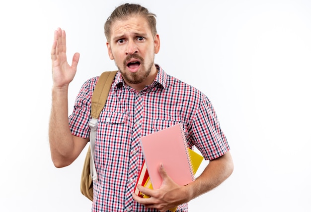 Scared young guy student wearing backpack holding books raising hand isolated on white wall