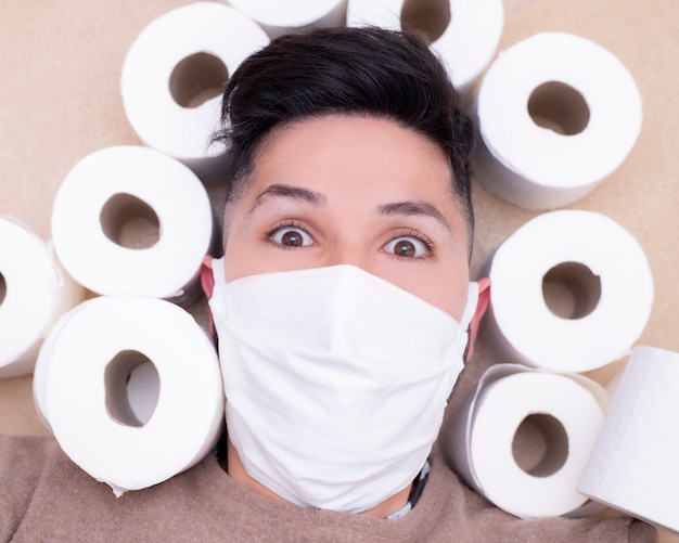 Scared young man with face mask on prevention surrounded by toilet paper.