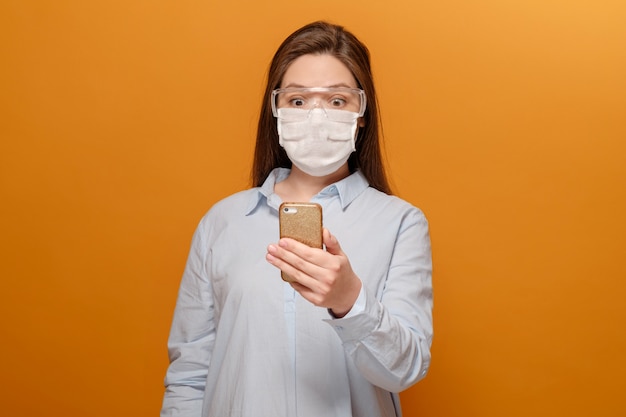 Scared young woman with medical mask on her face looks at phone, woman in panic over epidemic