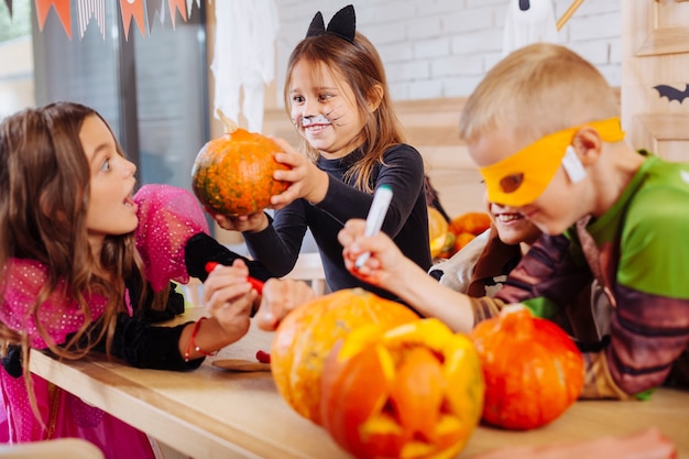 Scaring friend. Cute dark-haired girl with painted cat face scaring her friends celebrating Halloween together