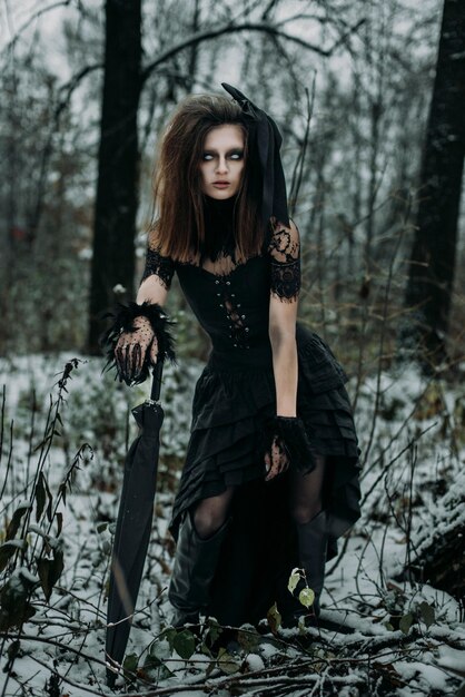 Photo a scary female figure of a witch in a black robe in an autumn forest an unsaturated image