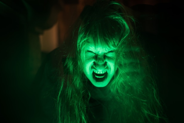 Scary ghost woman screaming through dirty glass on dark background