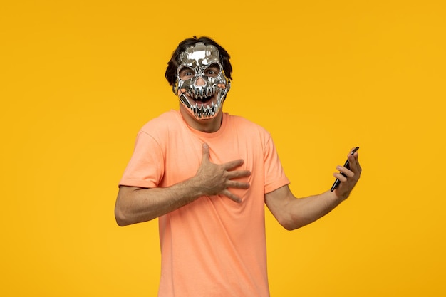 Scary mask terrifying cute guy laughing and holding a phone