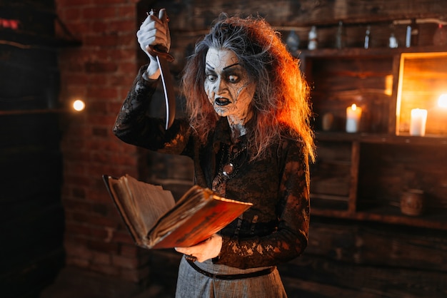 Scary witch holds spellbook and knife, dark powers of witchcraft, spiritual seance.