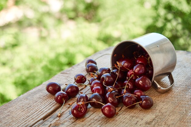 Scattered berries of red ripe cherry from a metal mug on a wooden background. The concept of summer food.