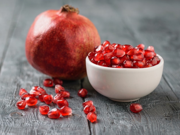 Scattered on a black table pomegranate seeds and ripe pomegranate. Vegetarian food.