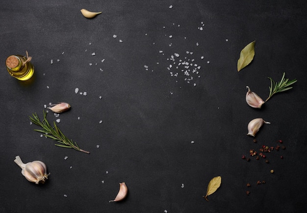 Scattered coarse white salt peppercorns and rosemary sprigs on a black table ingredients for cooking fish and meat