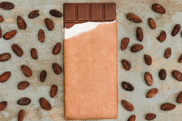 Scattered cocoa beans with chocolate bar on grunge background