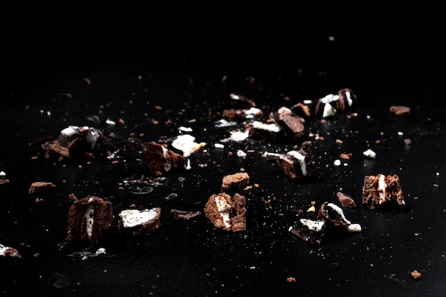 Scattered crumbs of chocolate sandwich cookies filled with sweet cream flavored isolated on black ba