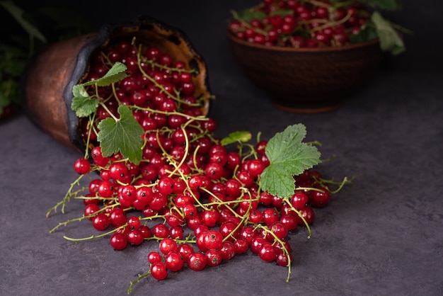 Scattered fresh berries of red currant on a dark background with leaves, summer ripe berries, close up.