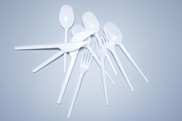 Scattered plastic forks knives spoons on a gray background close-up