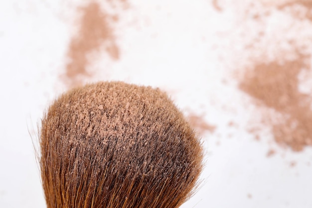 Scattered tan colored facial loose powder and makeup brush isolated on white background