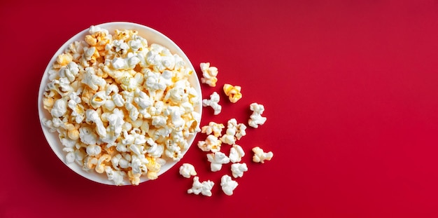 Scattered tasty cheese popcorn in bowl isolated on red background with copy space