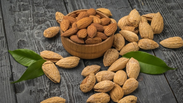 Scattered on a wooden table are unpeeled almonds and a wooden bowl with peeled almonds. Vegetarian food.