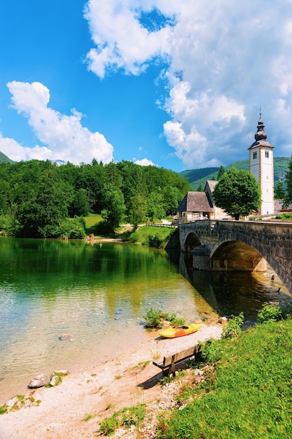 Scenery of canoe in Bohinj Lake, Slovenia. Nature and kayak in Slovenija. View of green forest and blue water. Landscape, Alpine Julian Alps mountains. John baptist church on background