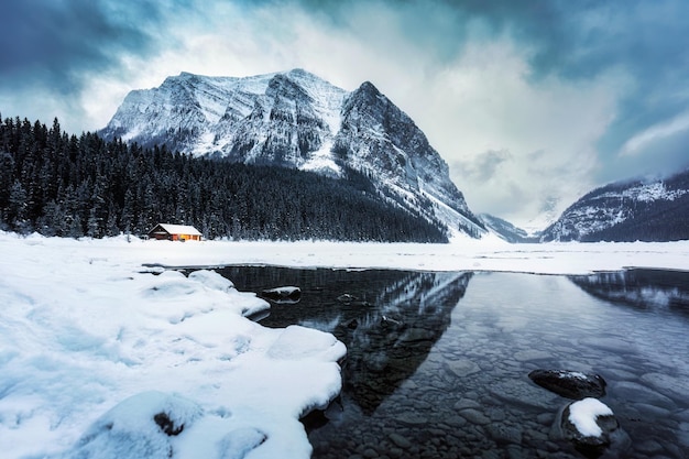 Scenery of Lake Louise with wooden cottage glowing and rocky mountains with snow covered in winter at Banff national park