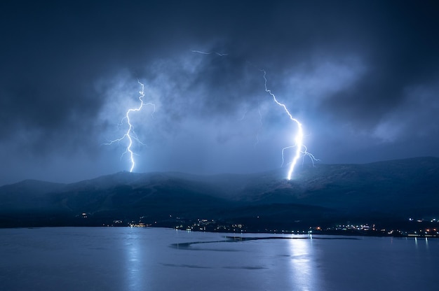 Scenery lightning strike during rainy storm hitting the mountain near lake