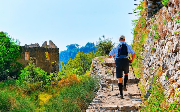 Scenery with man tourist on walk on Path of Gods in Italy at Naples. Amalfi coast and landscape with Tyrrhenian Sea at Italian Positano. Panorama of Amalfitana coastline in Europe. View in summer.