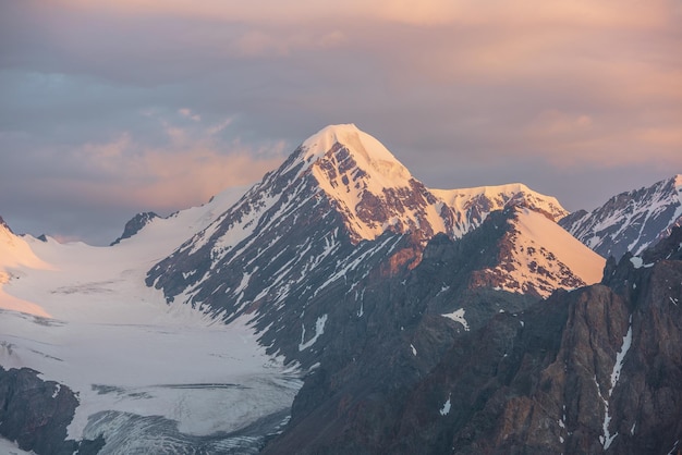 Scenic aerial view to high snow mountains in early morning at dawn Awesome scenery with sunlit gold pinnacle in cloudy sky at sunrise Morning landscape with snow mountain peak in golden sunlight