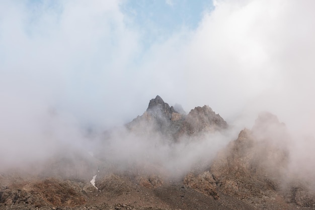 Scenic alpine landscape with rocky mountains in dense low clouds in morning sunlight Colorful mountain scenery with sharp rocks among thick low clouds Awesome view to high rockies in low cloudiness