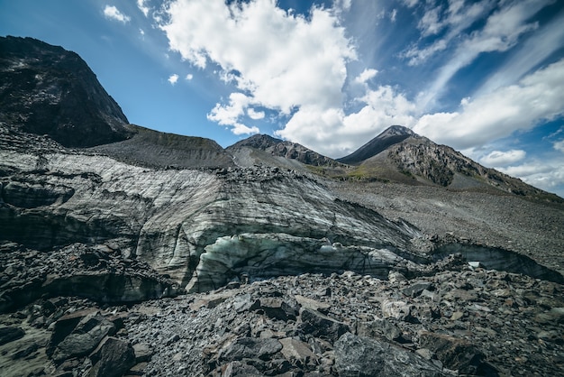 Scenic highlands landscape with big glacier and high mountain top in pyramid shape in sunny day. Awesome mountain scenery with icy hill with big stones and pinnacle. Glacier ice and stones in sunlight