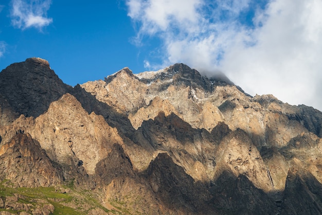 Scenic mountain landscape with great rocks in golden sunlight and low clouds. Awesome rocky wall with sharp top in gold sunshine. Colorful sunny scenery with high rocky mountain with pointed pinnacle.