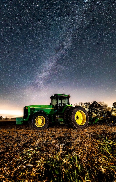 Scenic shot of a john deere green tractor in the middle of the agricultural field during the night