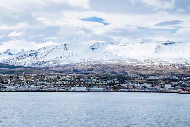 Scenic view of cityscape at seashore with snowcapped mountains in background