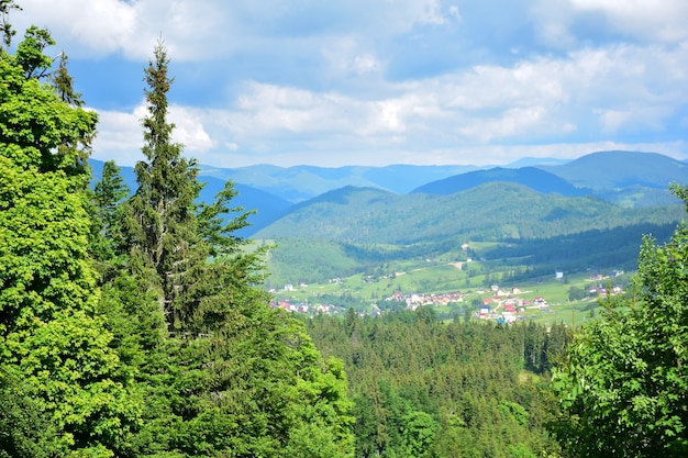 Scenic view from the mountain to the village between the mountains covered with summer forest. View from afar