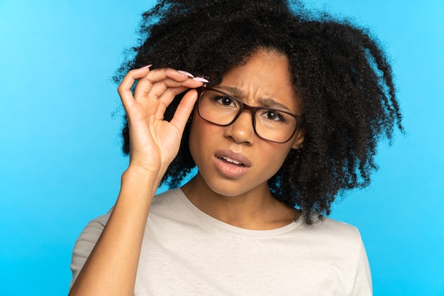 Sceptical mistrustful african american girl adjusts glasses suspicious looking at camera