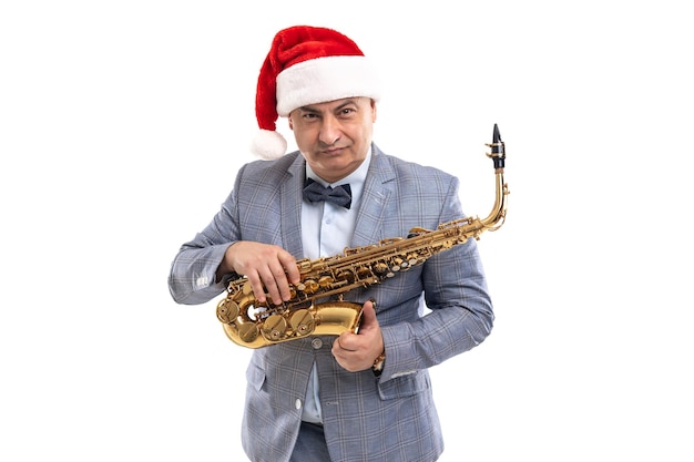 Sceptical musician man wears in santas hat holds saxophone over studio background