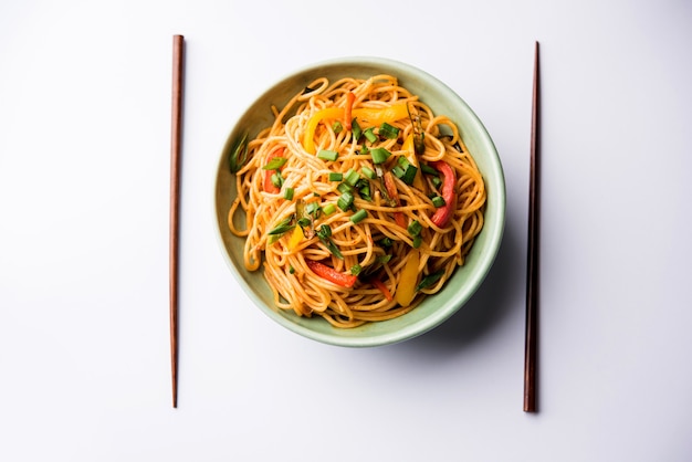 Schezwan Noodles or vegetable Hakka Noodles or chow mein is a popular Indo-Chinese recipes, served in a bowl or plate with wooden chopsticks. selective focus