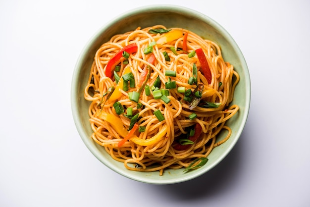 Schezwan Noodles or vegetable Hakka Noodles or chow mein is a popular Indo-Chinese recipes, served in a bowl or plate with wooden chopsticks. selective focus