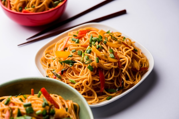 Schezwan Noodles or vegetable Hakka Noodles or chow mein is a popular Indo-Chinese recipes, served in a bowl or plate with wooden chopsticks. selective focus