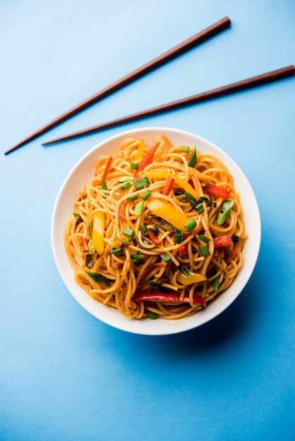 Schezwan Noodles or vegetable Hakka Noodles or chow mein is a popular Indo-Chinese recipes, served in a bowl or plate with wooden chopsticks