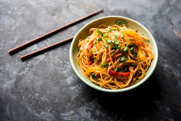 Schezwan Noodles or vegetable Hakka Noodles or chow mein is a popular Indo-Chinese recipes, served in a bowl or plate with wooden chopsticks