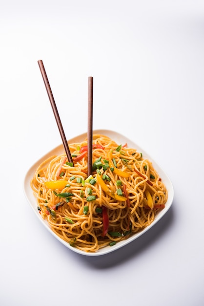 Schezwan Noodles or vegetable Hakka Noodles or chow mein is a popular Indo-Chinese recipes, served in a bowl or plate with wooden chopsticks