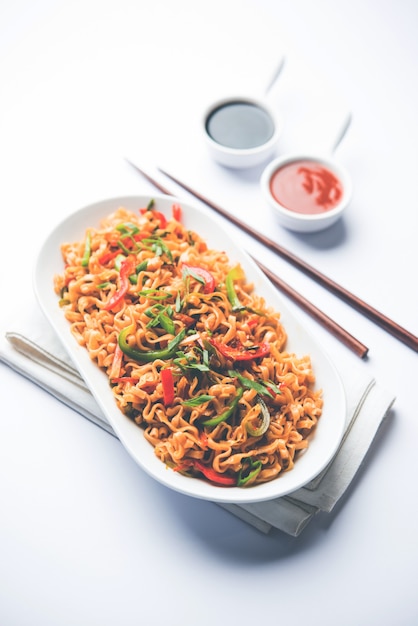 Schezwan veg noodles is a spicy and tasty stir fried flat Hakka noodles with sauce and veggies. served with chopsticks. selective focus